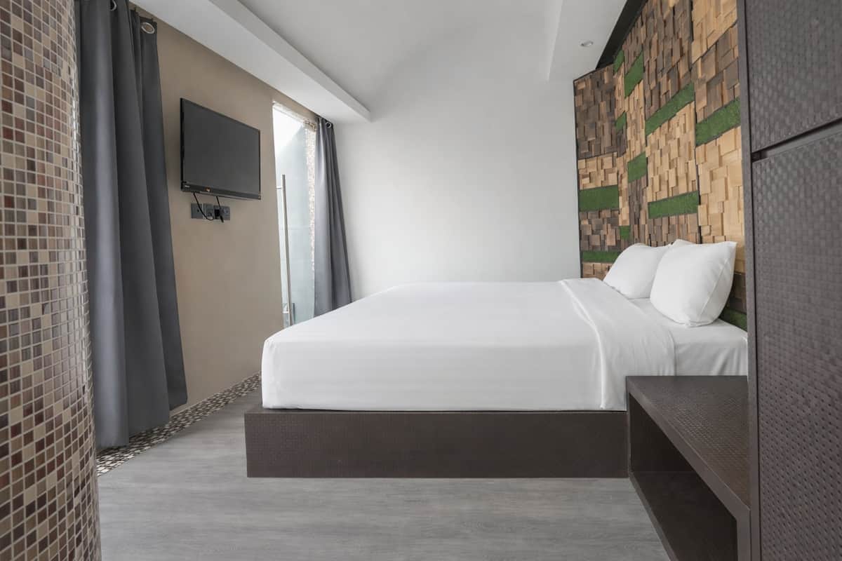 A modern hotel room with a large bed, a flat-screen TV mounted on the wall, and a unique wooden wall panel design.
