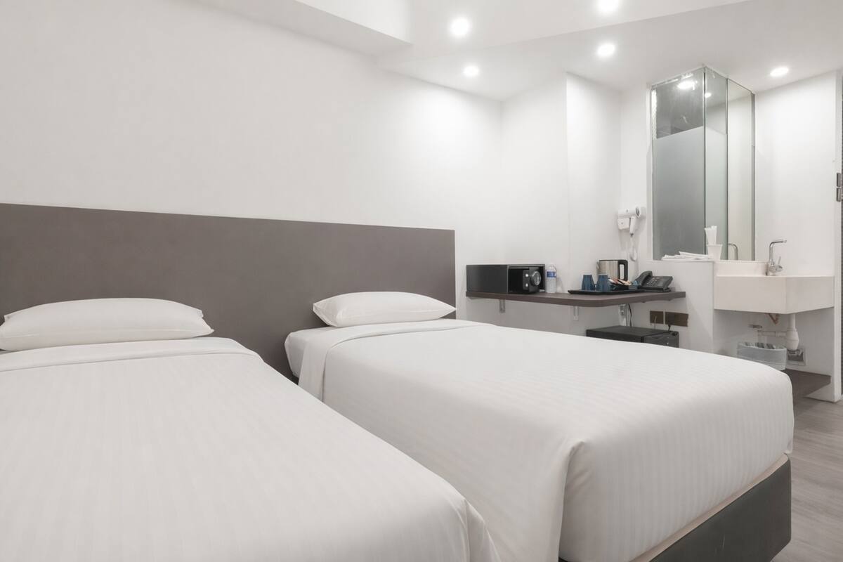 A hotel room with two beds, a large mirror, a sink, and a small table with a phone and a kettle.
