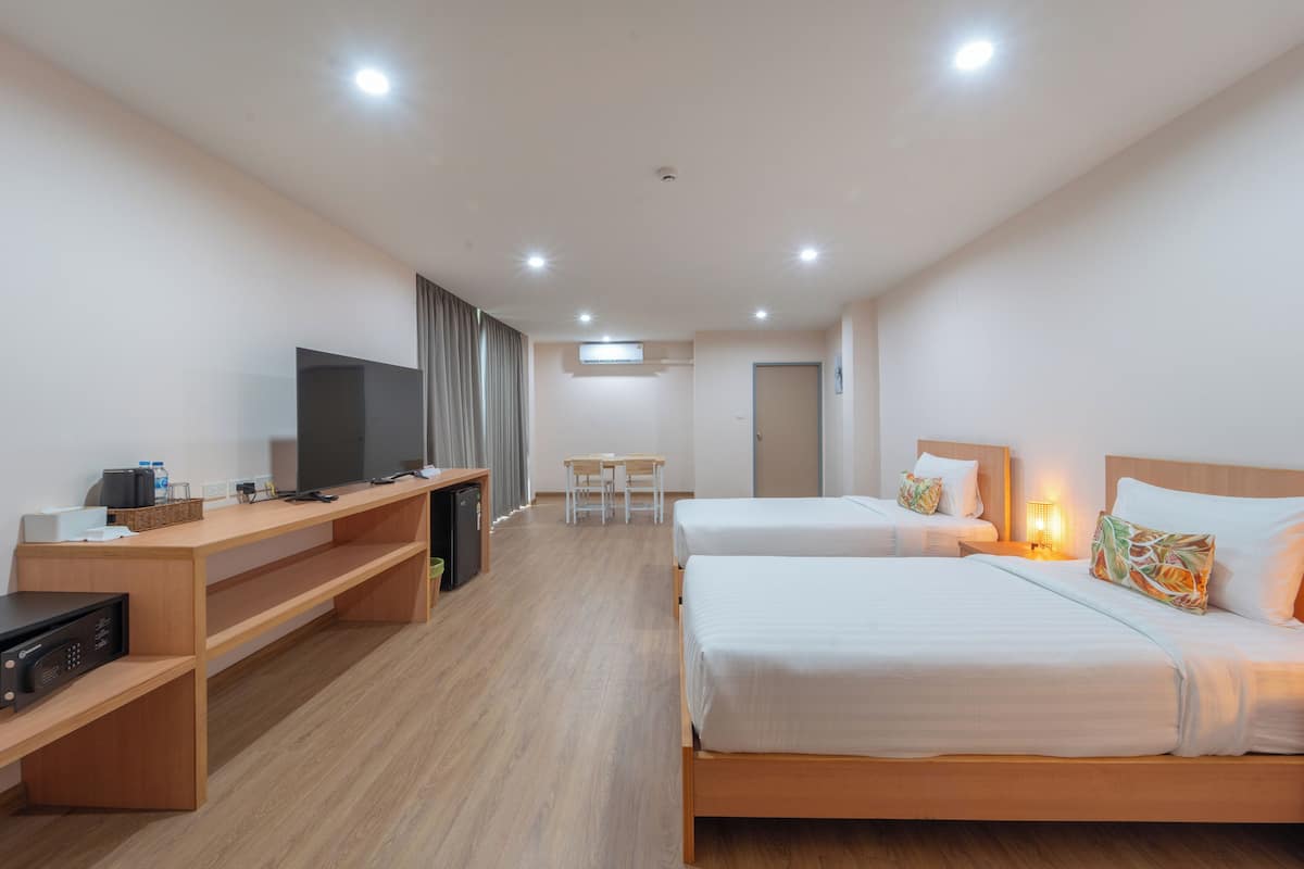 Quarto de hotel com duas camas, uma escrivaninha com televisão, uma mesinha e uma cadeira.