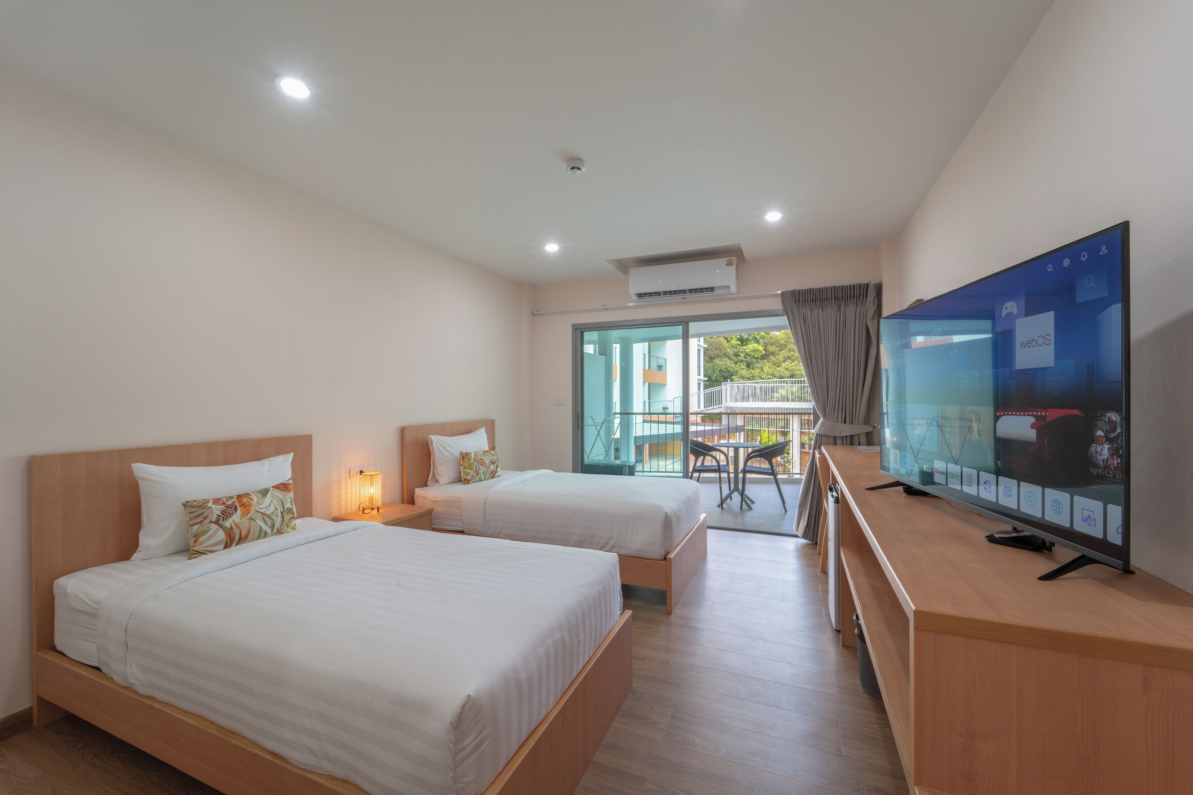A hotel room with two beds, a TV, and a balcony with a table and chairs.