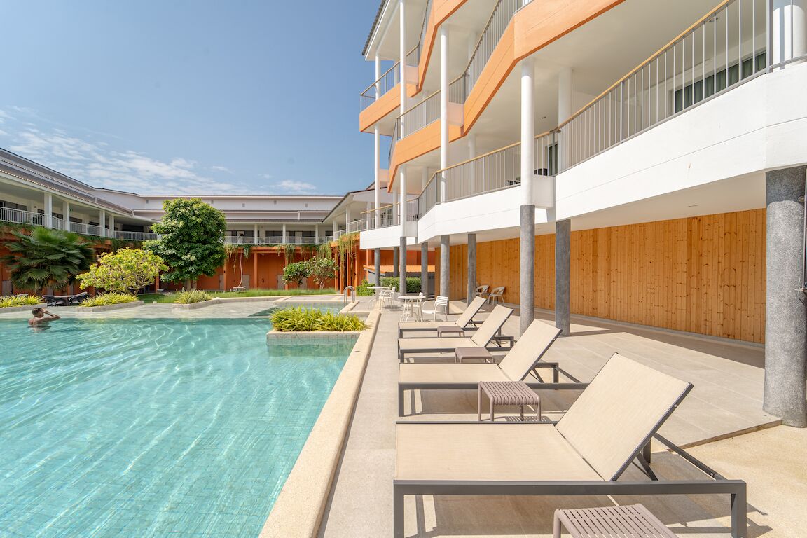 A modern hotel with a swimming pool, lounge chairs, and a wooden deck.