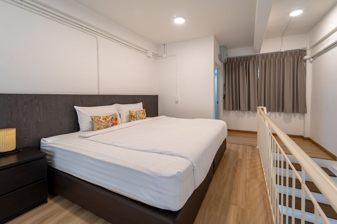 Een moderne slaapkamer met een groot bed, een nachtkastje, een lamp en uitzicht buiten door een raam met gordijnen.