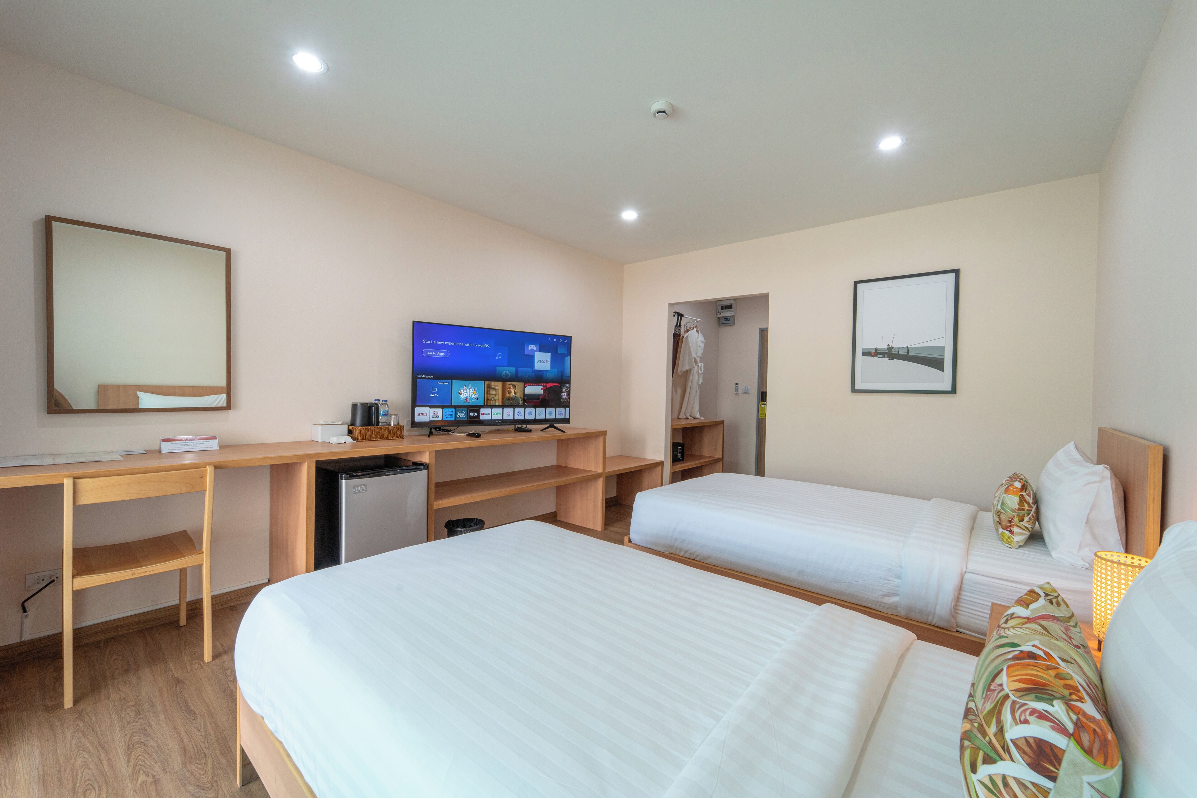 A hotel room with two beds, a desk with a computer, a TV, and a small kitchenette.
