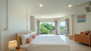 Een moderne hotelkamer met een groot bed, een sofa en een balkon met uitzicht op groen.