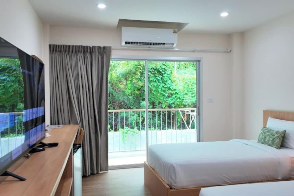Une chambre d’hôtel avec un lit, un téléviseur posé sur un bureau en bois et un balcon donnant sur un paysage verdoyant.