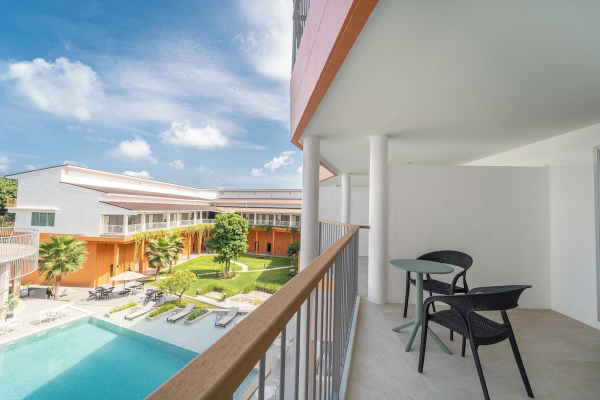 Varanda com piscina, área de estar externa e vista para um pátio com palmeiras e um edifício ao fundo.