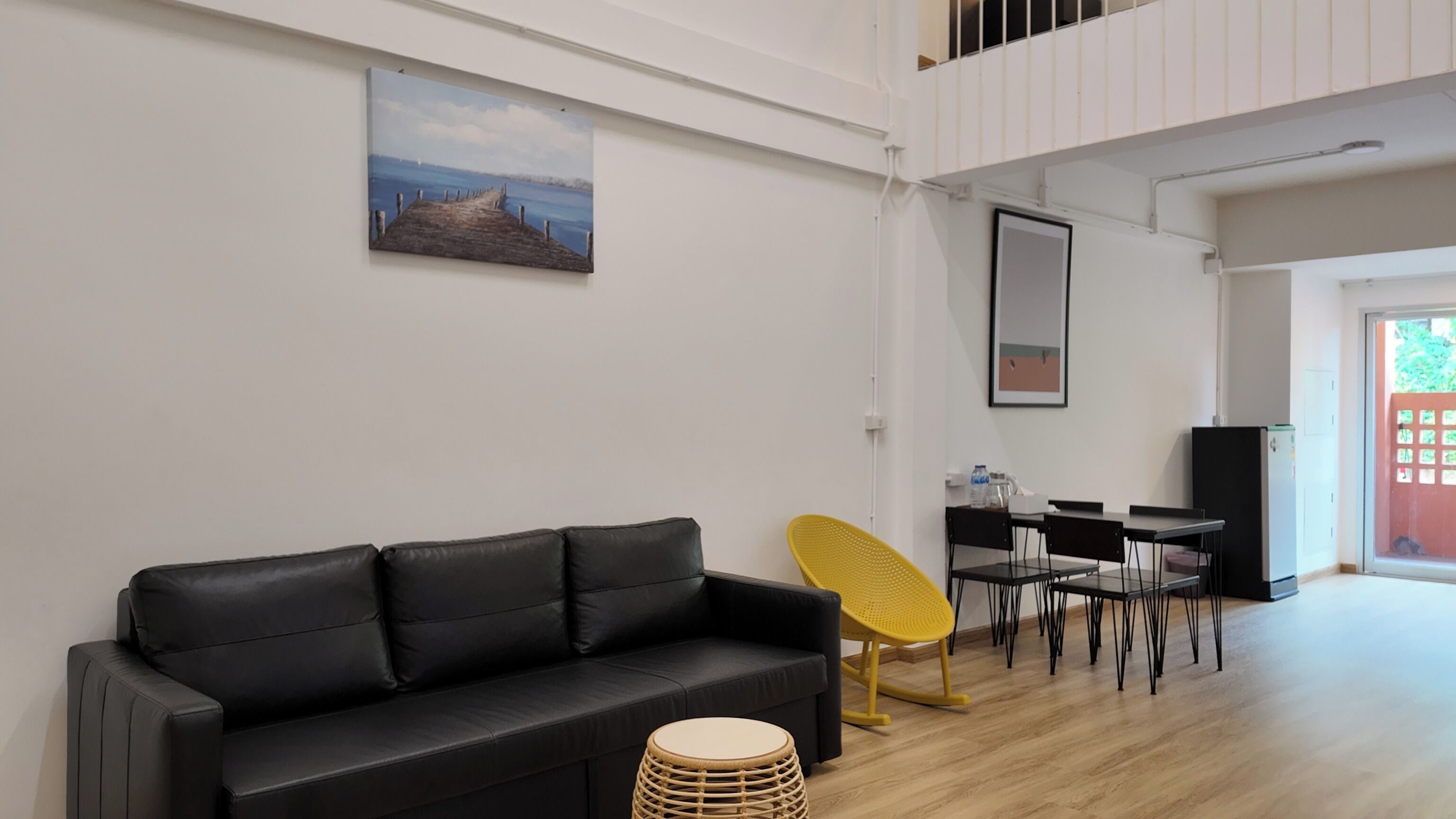 Un salon moderne avec un canapé en cuir noir, un fauteuil jaune et un coin repas comprenant une table et des chaises.