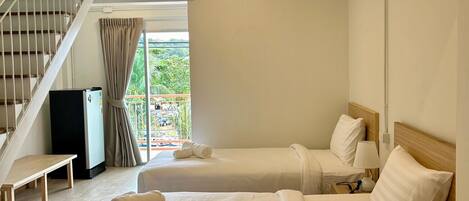 A hotel room with two beds, a wooden bench, a desk, a refrigerator, and a staircase.