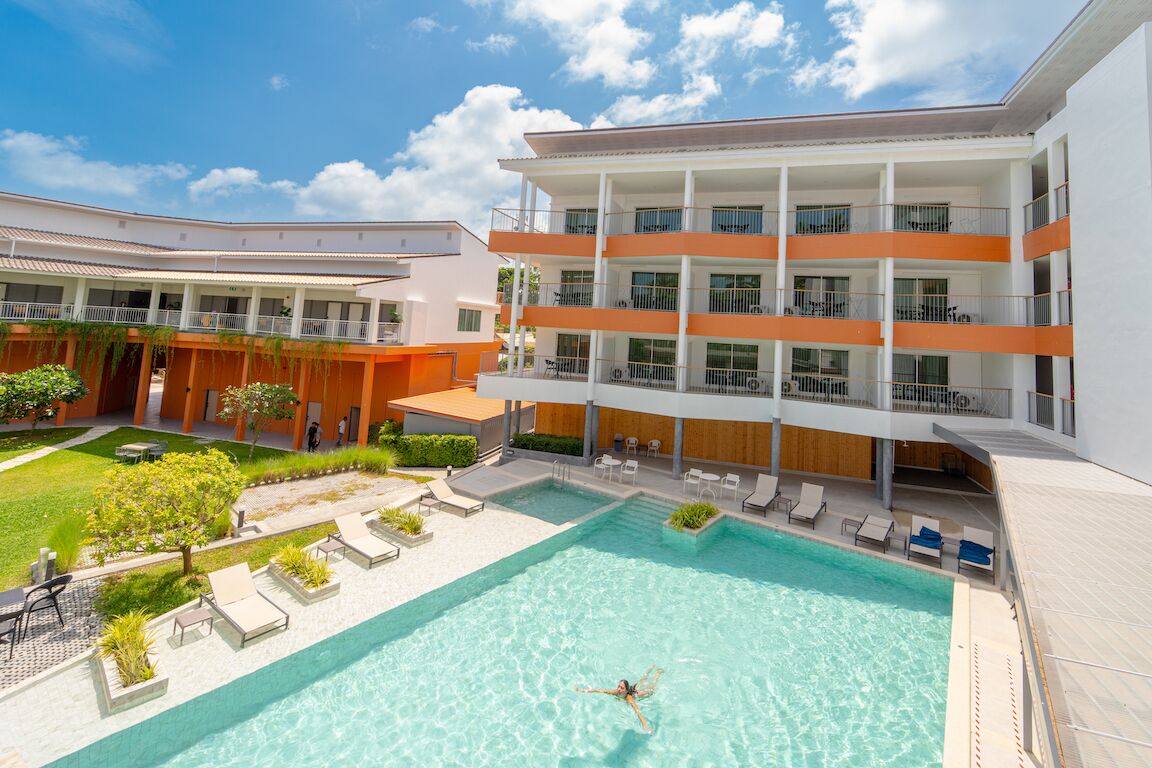 A modern hotel with a swimming pool, outdoor seating, and a multi-story building with balconies.