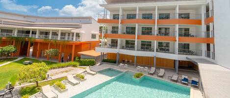 A modern hotel with a swimming pool, outdoor seating, and a multi-story building with balconies.
