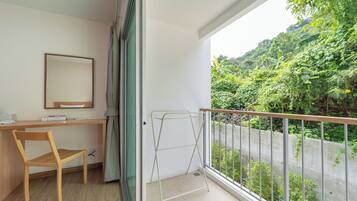 A balcony with a metal railing, a wooden chair, a desk with a mirror, and a view of lush greenery.