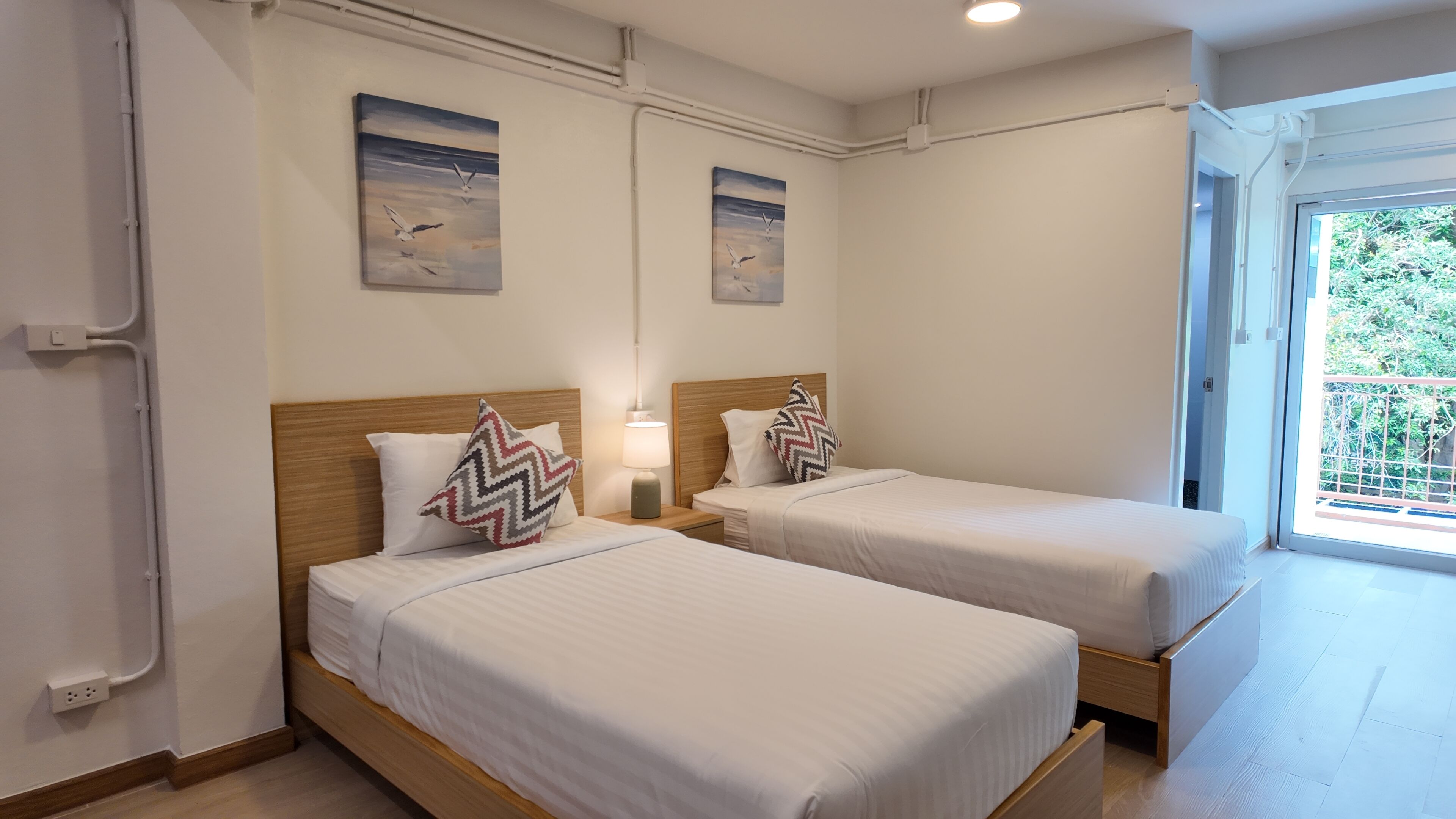 Une chambre d’hôtel avec deux lits simples, une table de chevet avec une lampe et deux tableaux accrochés au mur.