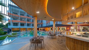 Een modern hotelinterieur met een centraal gelegen zwembad, meerdere eetgedeeltes en een bar.