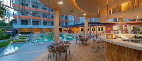 Et moderne hotelinteriør med en central pool, flere spisemiljøer og en bar.