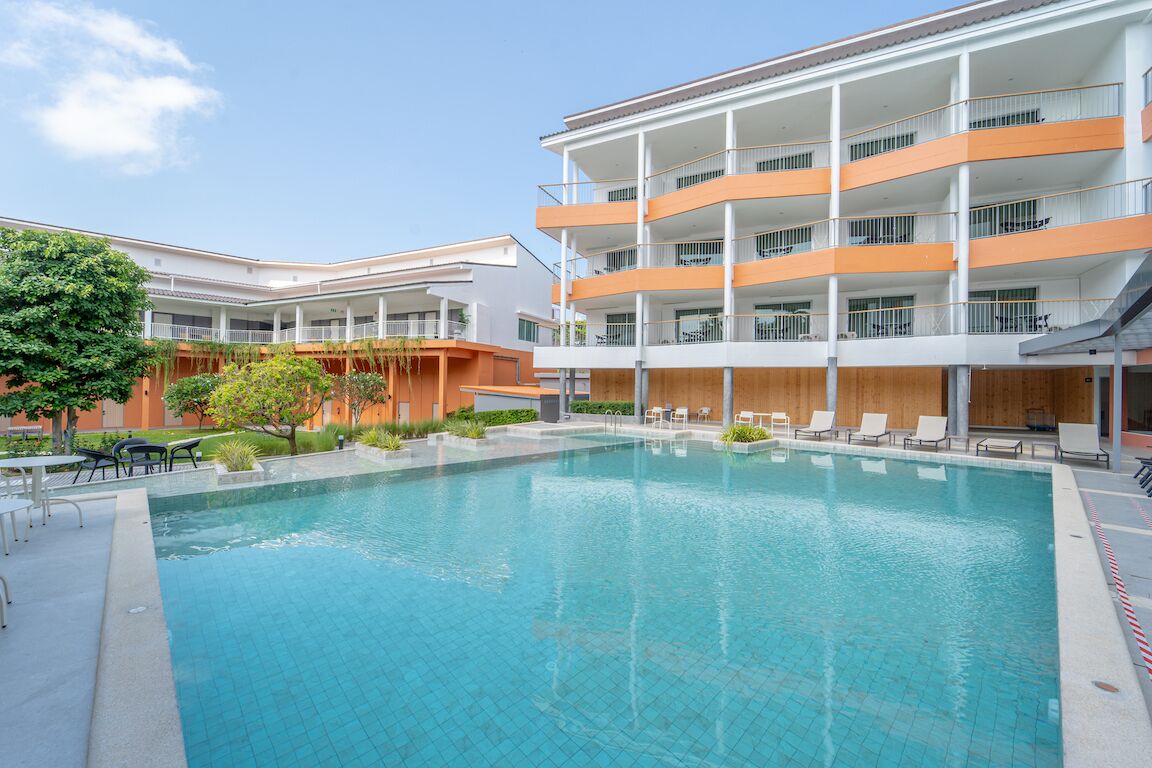Un hotel moderno con piscina, mobiliario exterior y un edificio de varios pisos con balcones.