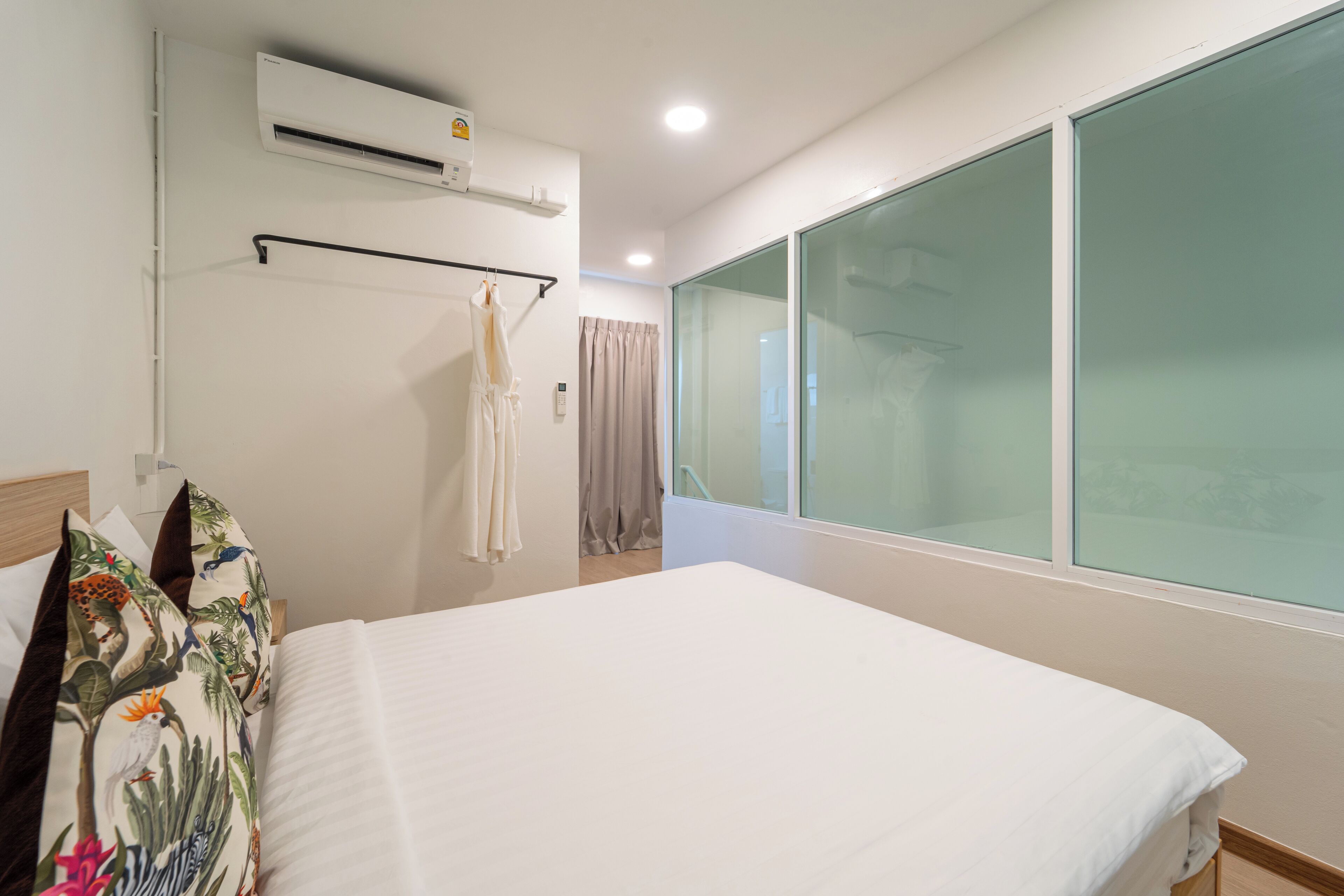 A hotel room with a large bed, an air conditioning unit, a window with a view, and a curtain.