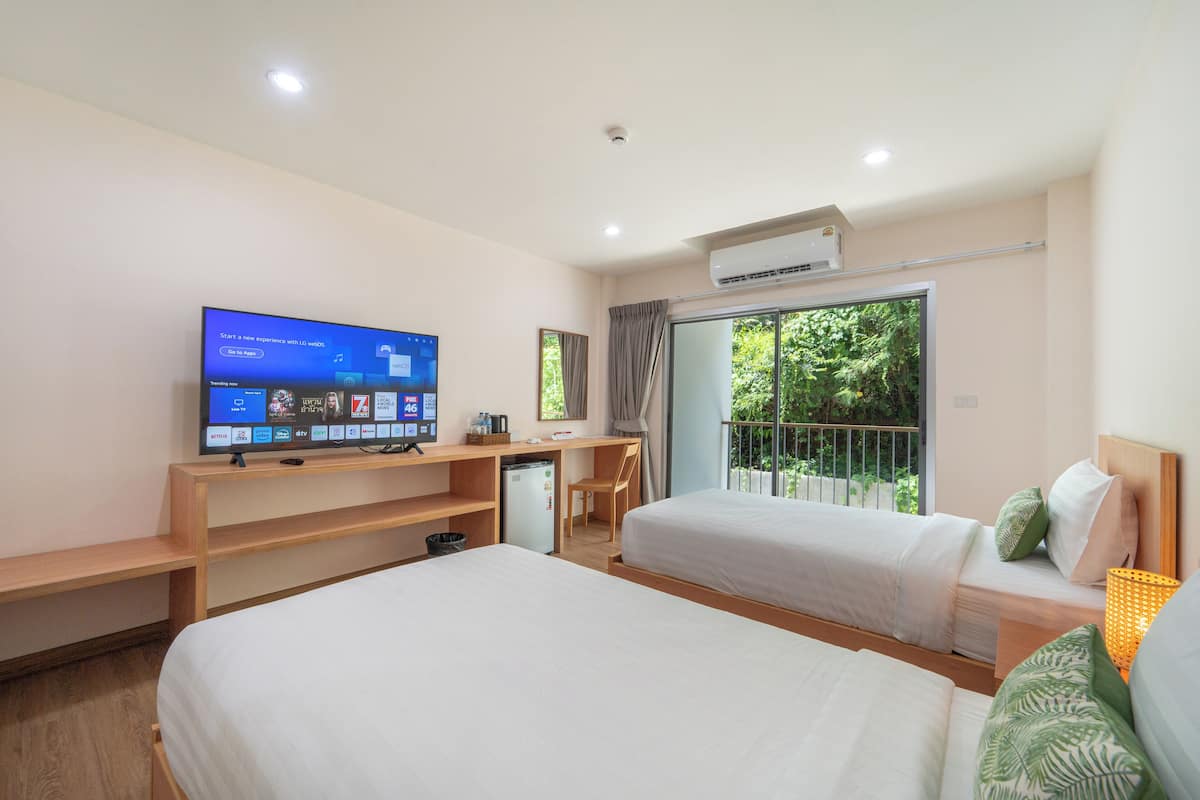 Quarto de hotel com duas camas, uma escrivaninha, televisão e varanda com vista para o verde.