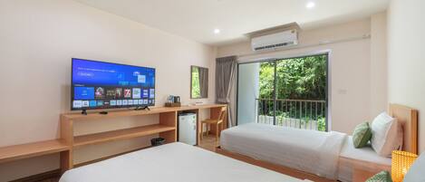 Habitación de hotel con dos camas, un escritorio, televisor y balcón con vista a zonas verdes.