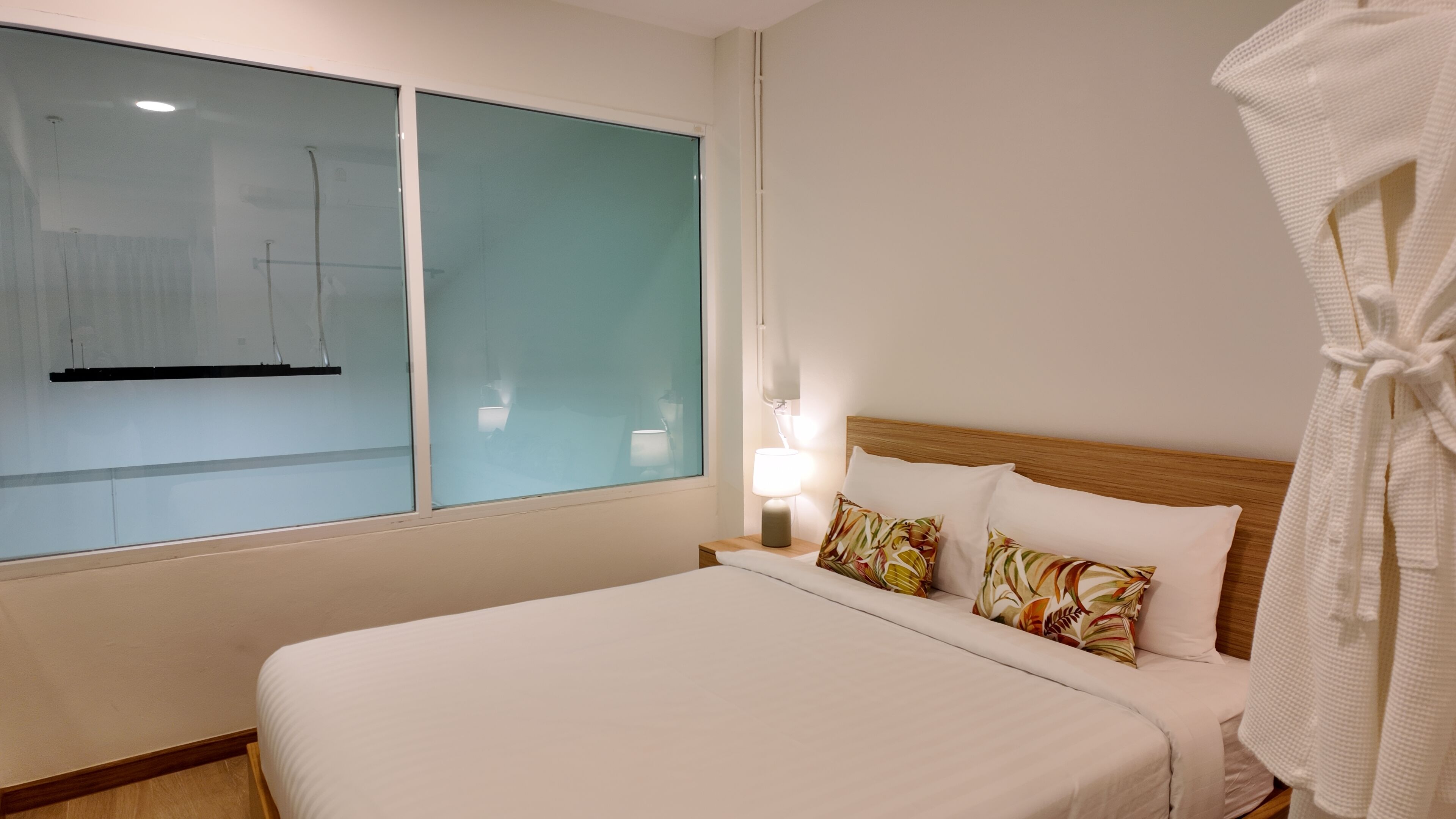 Una habitación de hotel con una cama grande, una mesita de noche con lámpara y un ventanal con vidrio esmerilado.