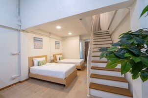 A hotel room with two beds, a staircase, and a potted plant.
