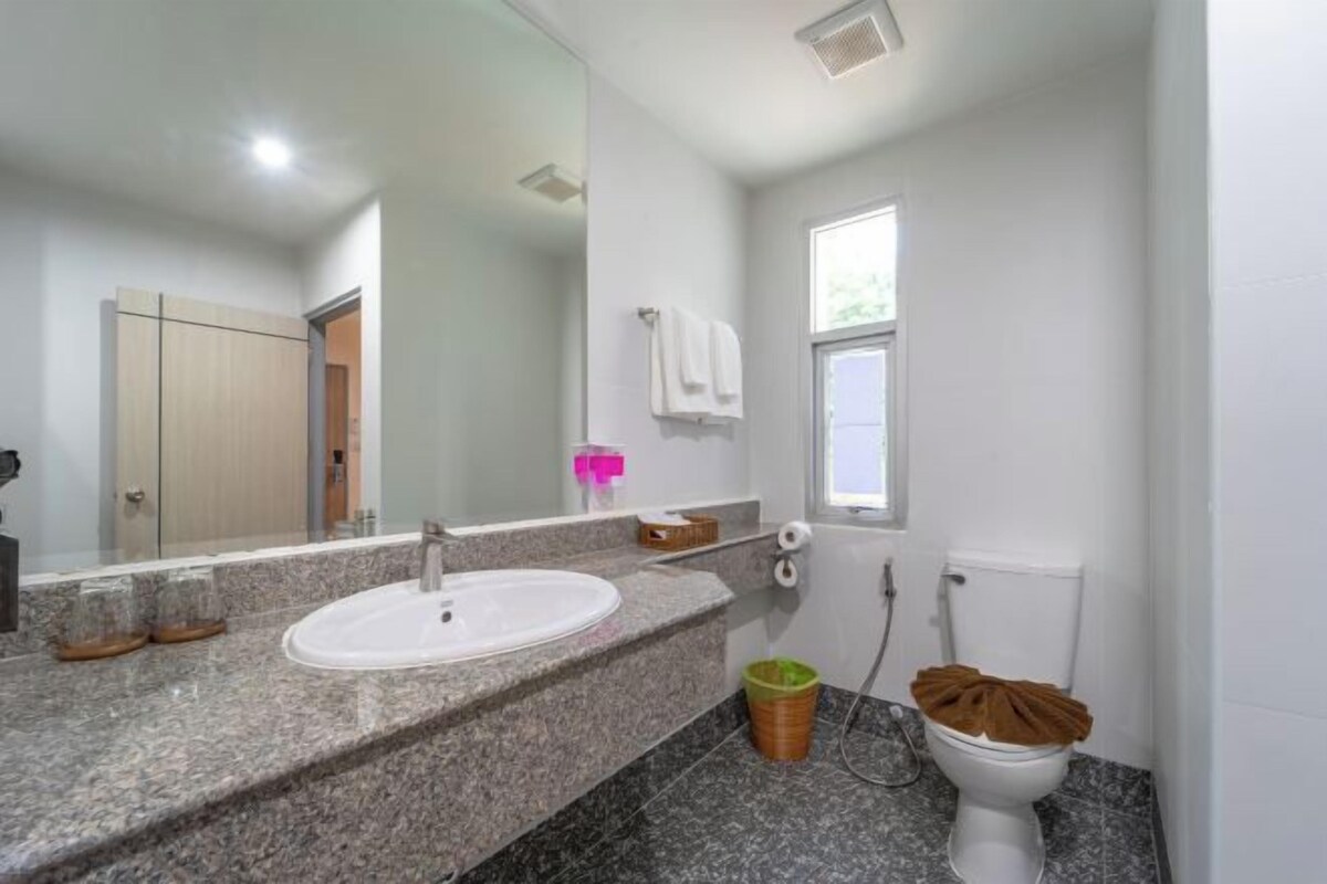 A bathroom with a granite countertop, a white sink, a mirror, a toilet, and a window.