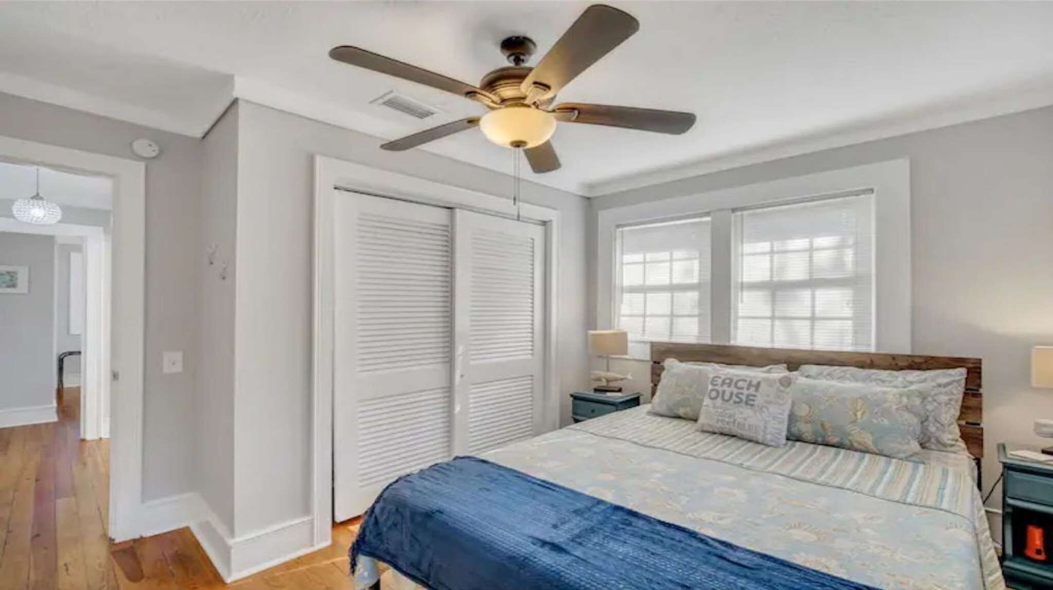 Une chambre à coucher avec un lit, un ventilateur de plafond, une table de chevet, une lampe et une fenêtre.