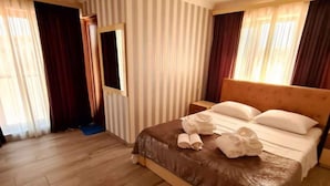 A hotel room with a large bed, wooden flooring, and striped curtains. - Dreamvilla tbilisi (Tbilisi)