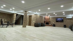 A spacious room with a high ceiling, recessed lighting, a fireplace, a flat-screen TV mounted on the wall, and a seating area with chairs and bean bags. - Dreamvilla tbilisi (Tbilisi)
