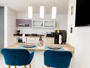 Een moderne keuken met een eethoek, inclusief een tafel met stoelen, een koelkast, magnetron en een aan de muur bevestigde televisie.