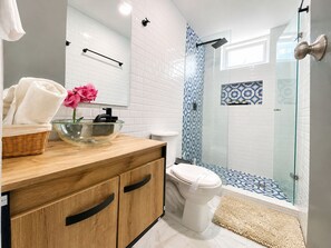 Une salle de bain moderne avec une douche à parois de verre, un meuble-lavabo en bois, des toilettes blanches et une fleur rose décorative.