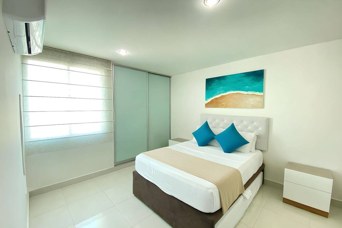 A bedroom with a bed, nightstand, and a painting of a beach scene.