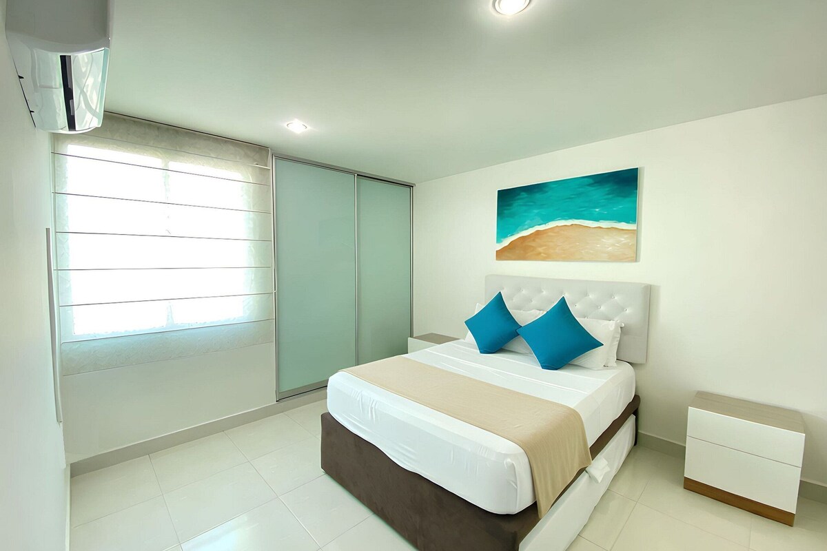 A bedroom with a bed, nightstand, and a painting of a beach scene.