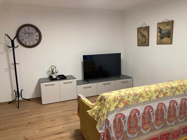 Un dormitorio con cama, televisor, perchero, reloj y dos cuadros en la pared.