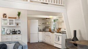 Een kleine keuken met witte kastjes, een koelkast, een fornuis en een eethoek met een tafel en stoelen.