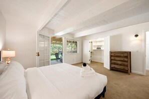 A bedroom with a bed, a nightstand, a lamp, a wooden dresser, and a view of the outdoors. - Lake Arrowhead Cabin 3BR | Hot Tub + Lake Access (Lake Arrowhead)