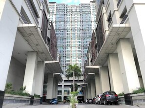 A multi-story residential building with a central entrance, surrounded by parked cars and a small palm tree.
