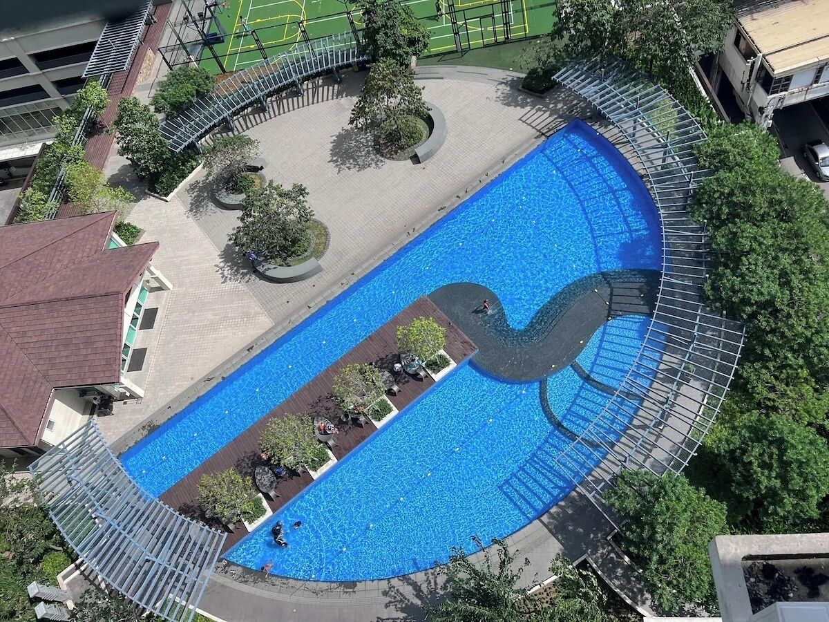 Vista aérea de una piscina con un diseño único, rodeada de árboles y un sendero pavimentado.