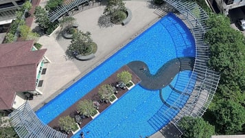 Vista aérea de una piscina con un diseño único, rodeada de árboles y un sendero pavimentado.