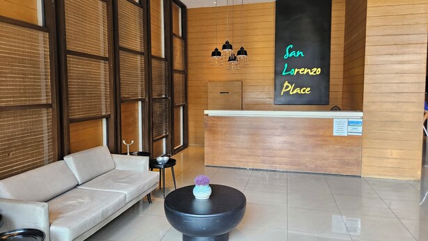 Een receptiegedeelte met een bank, een zwarte salontafel met een vaas, en een bordje met de tekst 'San Lorenzo Place'.
