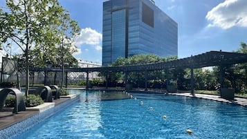 Una piscina con un puente, rodeada de follaje y un edificio moderno al fondo.