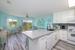 A modern kitchen with white cabinets, a large island, and a view of greenery outside. - Paradise Palms | 2 Balconies | Ocean Pointe 1206 (Tavernier)
