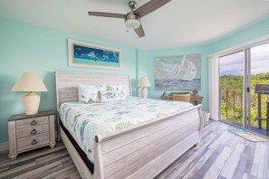 A bedroom with a bed, two nightstands, a ceiling fan, and a view of the outdoors through a sliding glass door. - Paradise Palms 2 Bedroom Condo Ocean Pointe 1206 (Tavernier)
