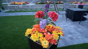 Un arreglo floral en una maceta en un patio con suelo de piedra y sillas al fondo.