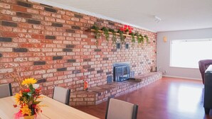 Una habitación amplia con chimenea de ladrillo, una mesa de comedor con sillas y un ventanal que ofrece luz natural.