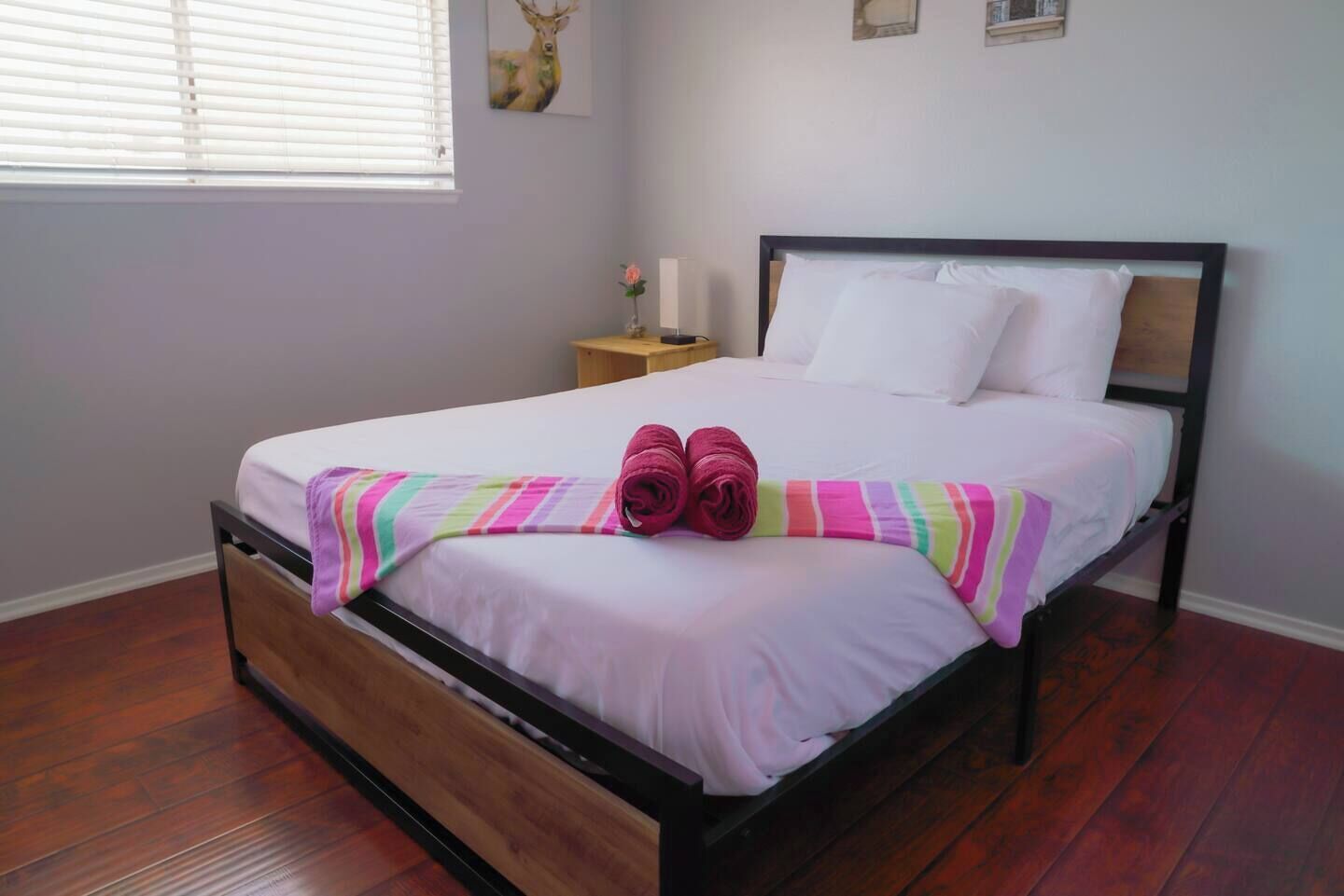 Un letto rifatto con cura, una coperta a righe, asciugamani arrotolati, un comodino in legno con una lampada e un quadro appeso al muro.