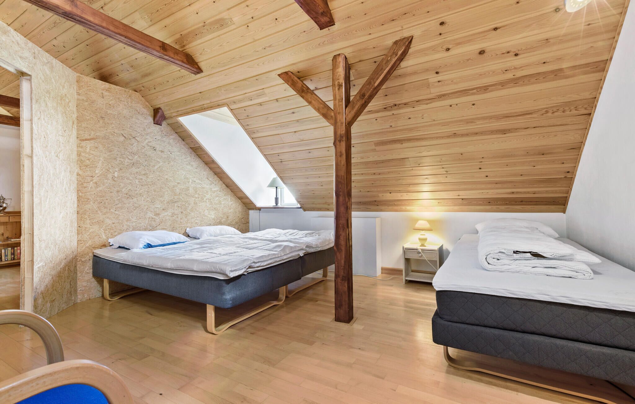 Ein Schlafzimmer mit zwei Betten, Holzbalkendecke, einem Oberlicht und einem Bücherregal.