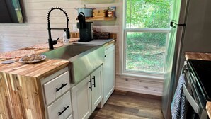 A modern kitchen with a wooden countertop, stainless steel sink, and a window with a view of greenery.