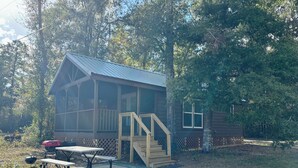 A rustic cabin with a porch, a picnic table, and a barbecue grill.