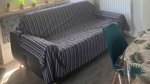 A cozy room with a striped sofa, a small table with plants, and a window with curtains. - Péniche Marie-lou (Thourotte)
