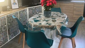 A modern kitchen with a large flat-screen TV, a dining table with teal chairs, and a decorative vase with red flowers. - Péniche Marie-lou (Thourotte)